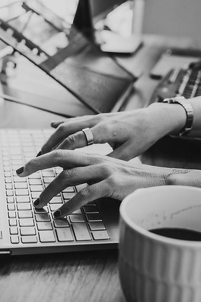 Typing on a keyboard in black and white, at West St. Studio, a natural light studio available for rent in Port Colborne, ON, with white walls, floor to ceiling windows, original floors, modern with historic charm.