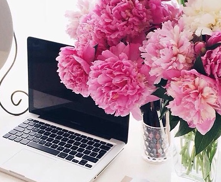 Laptop on desk with peonies in crystal vases