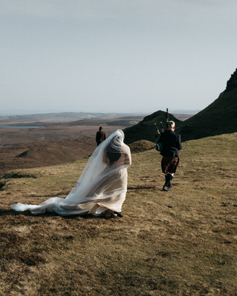 Bride walking to the ceremony while bagpiper plays at Quiraing, Skye