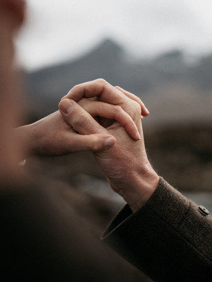 Close-up of the bride and groom's clasped hands with the Cuillin Mountains softly out of focus