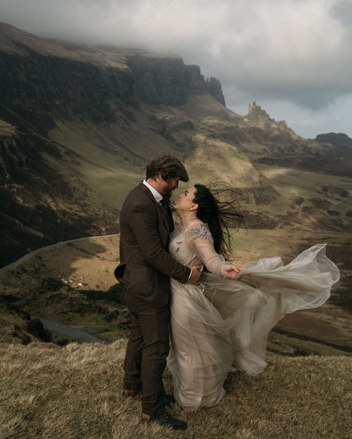 Groom holding bride as dress blows in the wind at the Quiraing, Isle of Skye