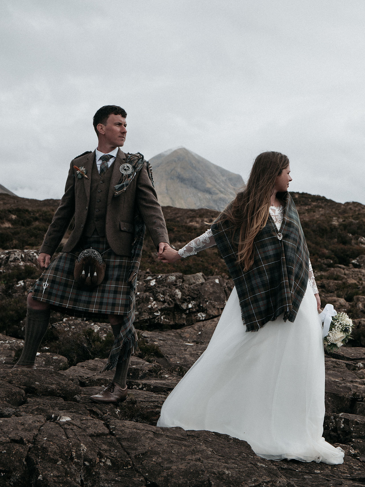 Bride and groom holding hands while looking towards the Cuillin Mountains