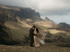 Windswept bride and groom embracing in dramatic scenery on the Isle of Skye