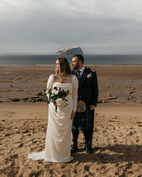 Married couple standing on Scottish beach looking towards the sun