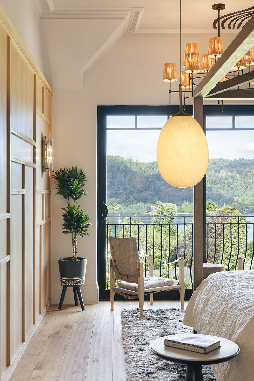Bedroom with timber wardrobes, a lounge chair and glazing overlooking the lake.