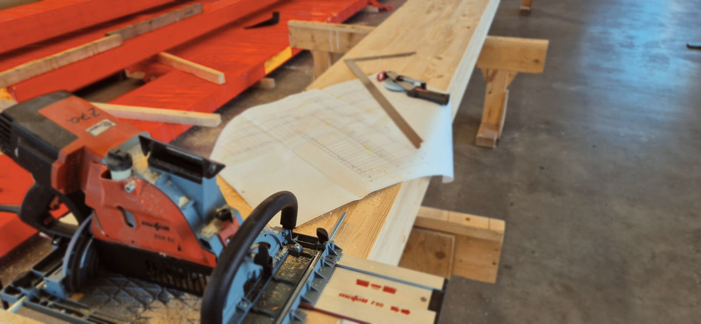 Ein Holzbau Gerät, ein Plan mit Lineal und Werkzeug liegen auf einem Holzbalken oder Werkbank in einer Lagerhalle
