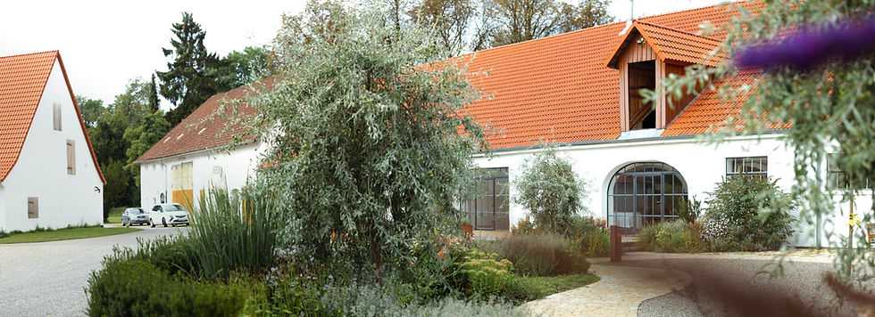 Weißes Gebäude mit rotem Ziegeldach und Bäumen im Hintergrund.