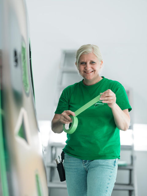 Eine Mitarbeiterin klebt Flächen für das Lackieren ab