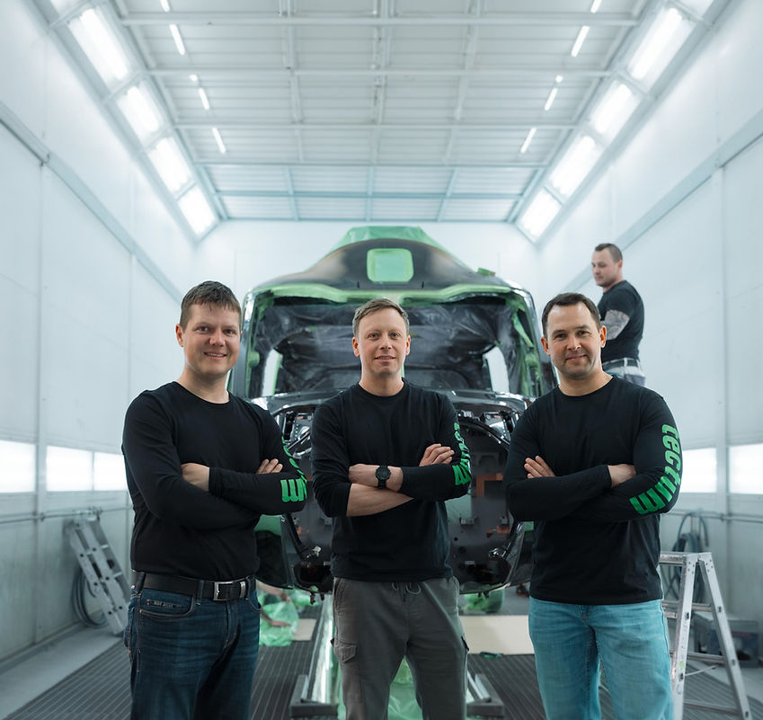 Mitarbeiter stehen vor einem Bauteil in der Lackierkabine