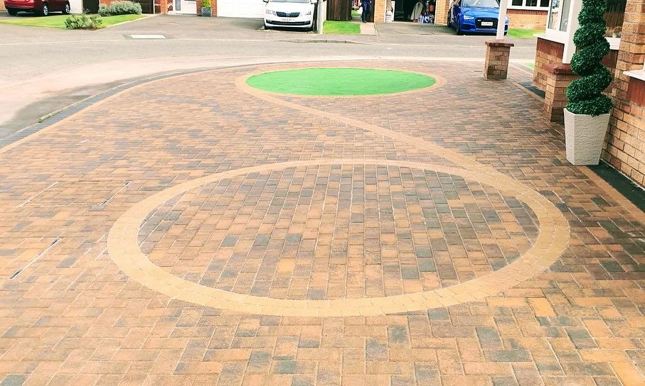 Brick driveway with a circular design and a small patch of artificial grass