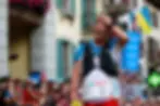 Courtney Dewaulter in blue and white gear, hand on head, excited expression in busy marathon race setting. Crowd and flags in background. UTMB bib visible.