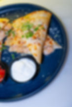 Quesadilla wedges topped with herbs and cheese on a blue plate, with sour cream and salsa sides. Creamy, appetizing appearance.