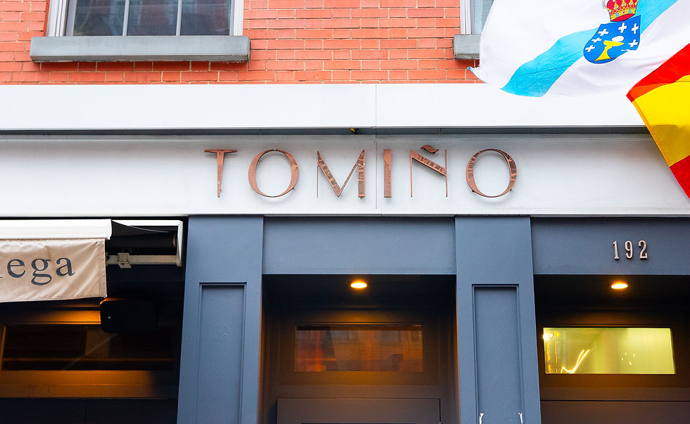 Facade of Tomiño restaurant with brick wall, blue details, flags, and address 192. Warm lit entrance, inviting ambiance.