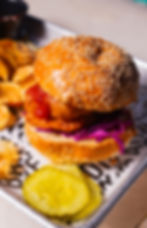 Sesame seed bun burger with crispy chicken, red cabbage, and sauce. Served with chips and pickles on a tray with text background.