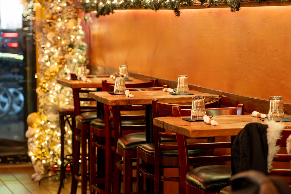 Cozy restaurant with wooden tables and chairs, adorned with festive lights and ornaments. Glasses and napkins are set; a warm ambiance prevails.