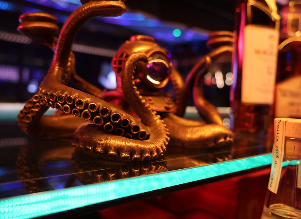 Bronze octopus sculpture on a glass shelf with colorful lights. Bottles visible in the background. Vibrant, nautical-themed setting.