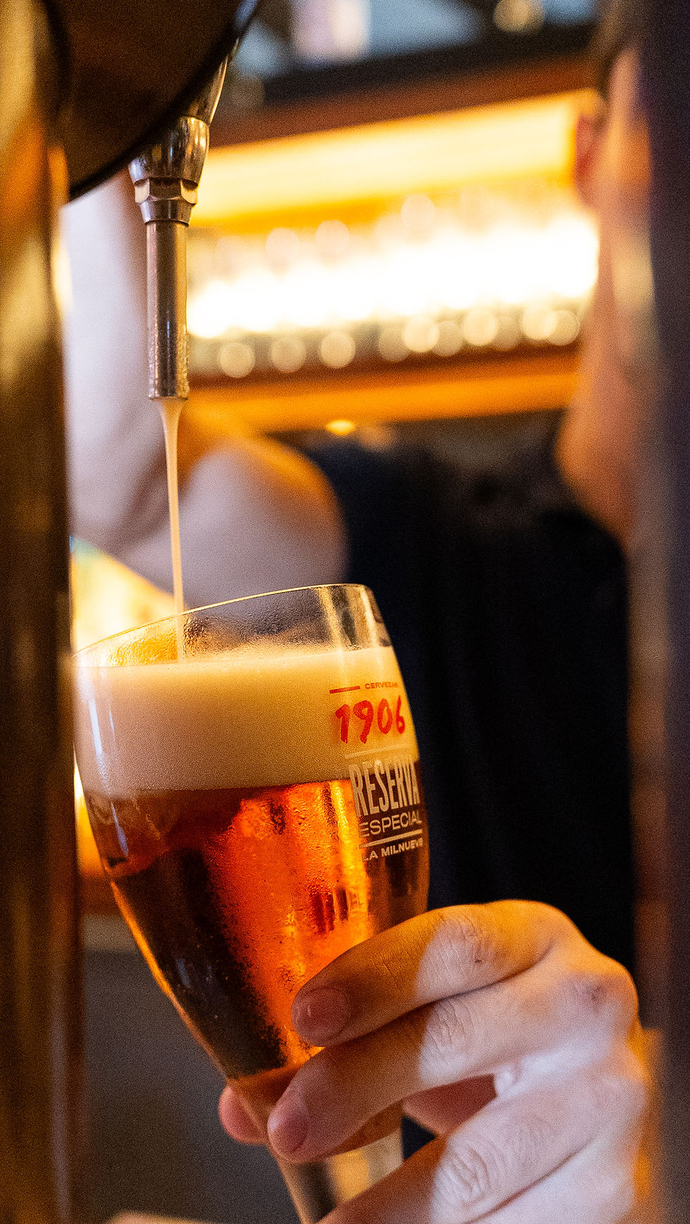 Pink cocktail with an orange slice and straw on a tray in a dimly lit bar, surrounded by other drinks. Mood is vibrant and lively.