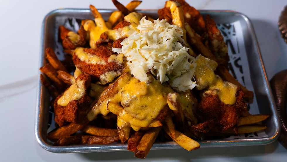 Fries topped with crispy chicken, melted cheese, and shredded cabbage on a silver tray. The setting is a neutral-toned tabletop.