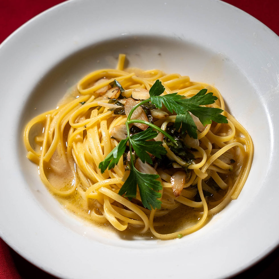 A plate of spaghetti with garlic, herbs, and parsley garnish. The dish is on a white plate against a red background.