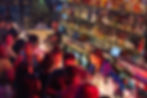 Crowded bar scene with people socializing and bartenders serving drinks. Colorful bottles line the shelves, creating a lively atmosphere.