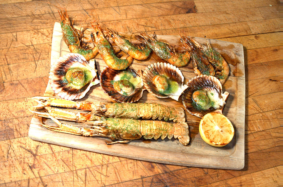 Seafood platter on a wooden board with shrimp, scallops, and langoustines, garnished with herbs, set on a rustic wooden table.