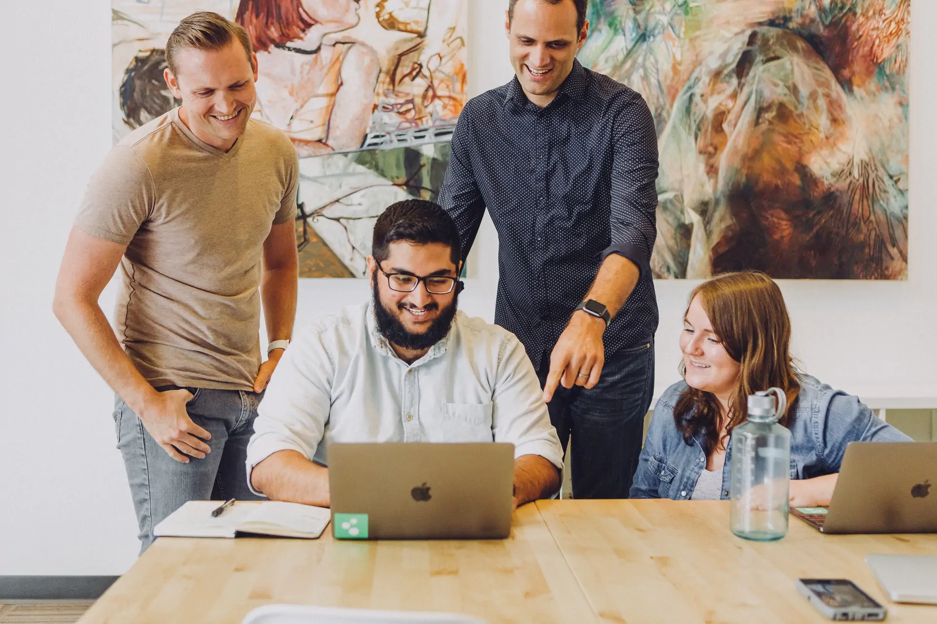 Three men are looking at the laptop in the office and smiling.