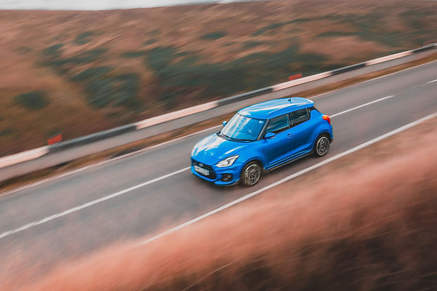 Suzuki Swift Sport Review - high angle front three quarter panning shot with the Peak District as the backdrop