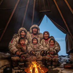 Nenets reindeer herding family portrait inside traditional chum tent with firelight, wearing malitsa