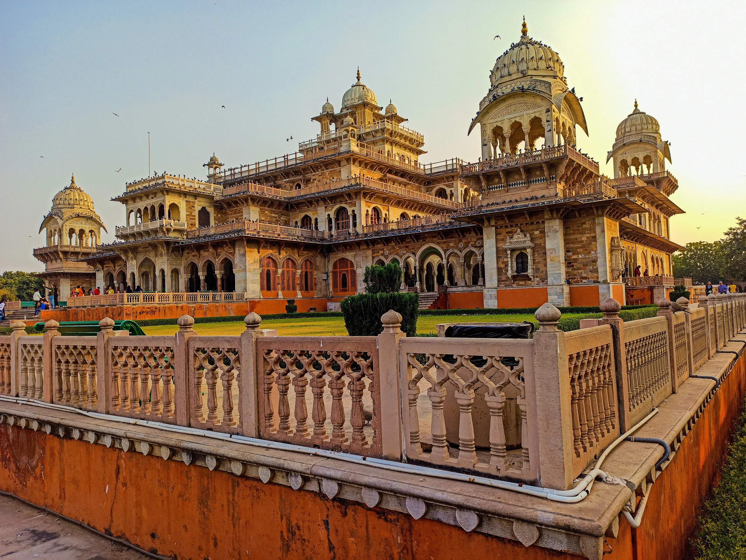 Albert Hall Museum – The Jewel of Jaipur with Christone Holidays : A majestic twilight view of Albert Hall Museum, Jaipur’s oldest museum, illuminated against the indigo sky. Its Indo-Saracenic arches and domes glow warmly, while Christone Holidays guests admire the intricate façade featuring Ramayana frescoes, Mughal-style minarets, and European clock towers. The foreground captures the museum’s reflection in the Apex Court water tank, doubling its grandeur. Architectural Marvels: Central Dome inspired by London’s Victoria & Albert Museum Jharokha balconies with delicate stone latticework Egyptian motifs blending with Rajput craftsmanship Ceramic tile murals depicting global civilizations Christone Holidays’ art historian decoding the façade’s hidden stories.Golden Hour Magic: 6:00-7:00 PM when 1,500 bulbs light up the exterior (Oct-Mar),Did You Know? The foundation stone was laid by Prince Albert during his 1876 India tour, Jaipur museum tours with Christone Holidays