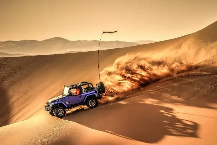 Thrilling jeep safari adventure across Jaisalmer's golden sand dunes with Christone Holidays, showcasing powerful 4x4 vehicles climbing steep desert slopes under bright blue skies. Excited tourists cheer as the jeep navigates dramatic Thar Desert terrain, creating clouds of golden sand in its wake. This action-packed scene highlights our Rajasthan desert safari packages, featuring professional drivers, dune bashing experiences, and stops at remote desert viewpoints. Perfectly captures the adrenaline of off-roading in Sam Sand Dunes while maintaining safety standards. Book your Jaisalmer jeep safari with Christone Holidays for an unforgettable combination of adventure and stunning desert photography opportunities at sunset." Conquer the dunes in style"!