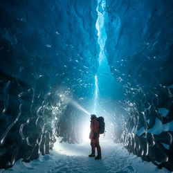 Inside glacial ice cave on Franz Josef Land with explorer illuminating deep blue ice crystal formati