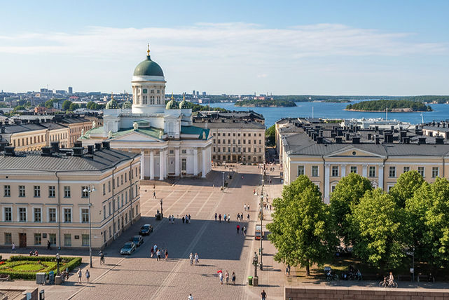 Helsinki cityscape with a white cathedral above a large square, coastal islands in the distance, and calm sea under a bright sky