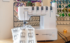 Machine à coudre Brother Cover Stitch CV3550 sur un plan de travail, avec un tissu personnalisé "Édition Limitée Handcrafted" en cours de couture. En arrière-plan, un porte-bobines garni de fils multicolores.