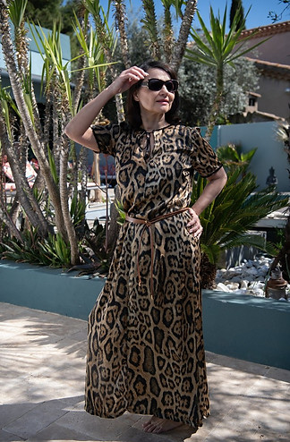 Femme debout en robe léopard, posant avec assurance sous les palmiers et levant la main vers le soleil.