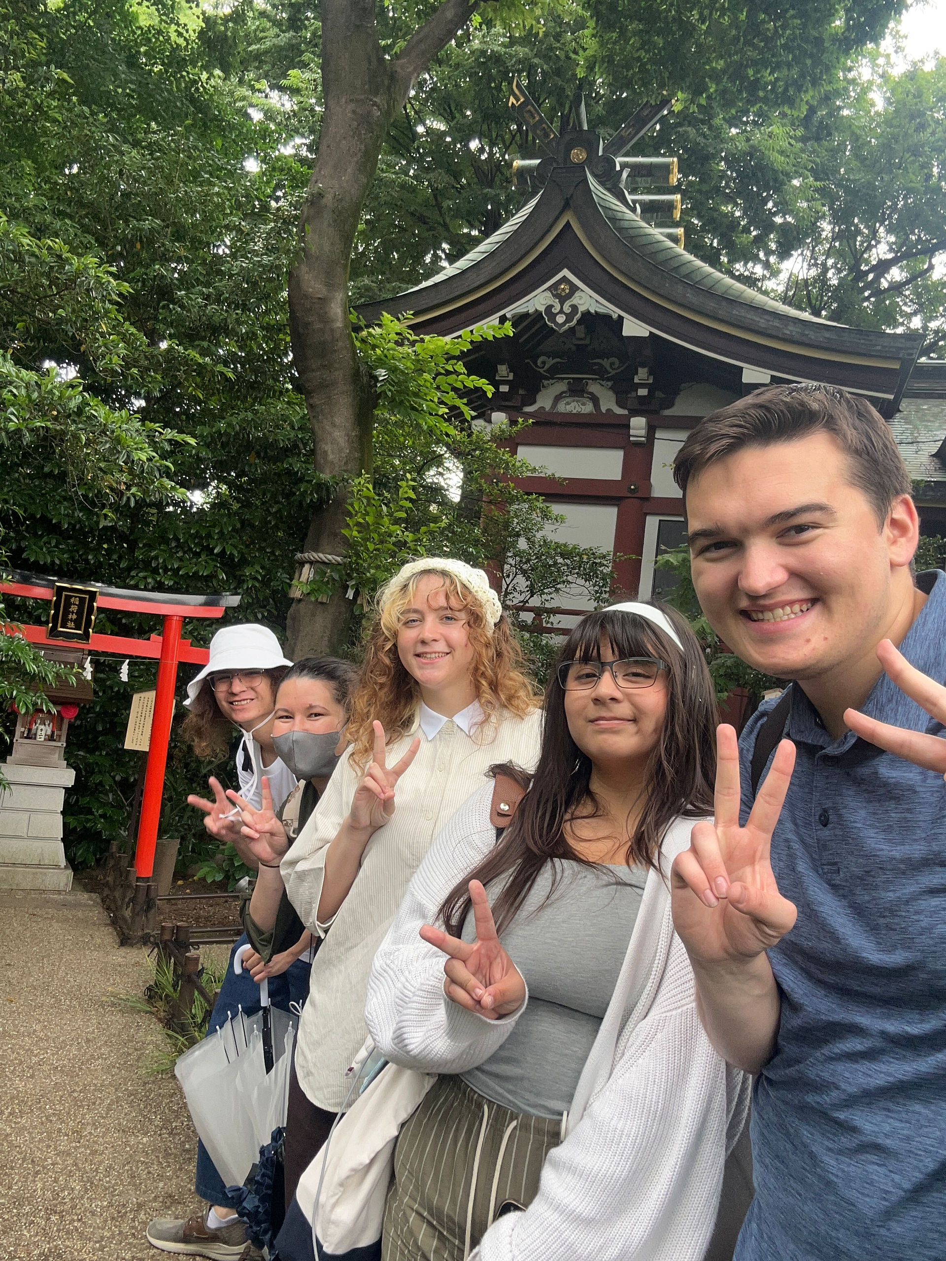 Several students giving a peace sign in front of a shrine of fortune in Hakone
