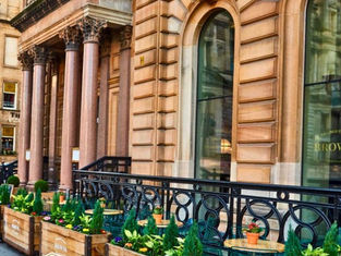 Street view of a historic stone building with large columns, arched windows, and Brown's Brasserie and Bar logo. Planters with greenery and flowers line the sidewalk.