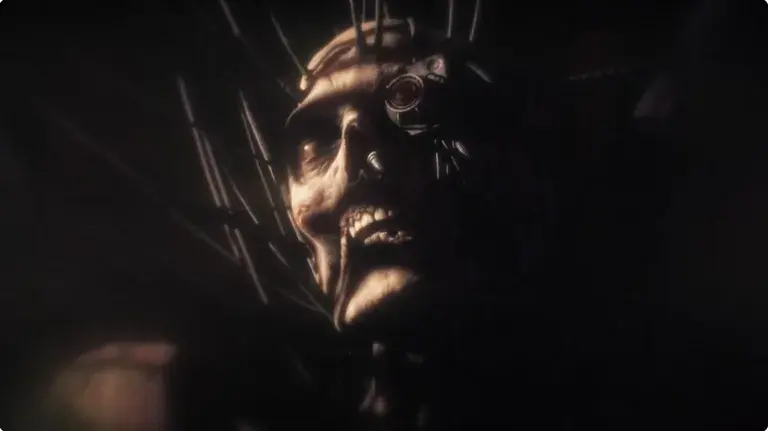 Screenshot of the Emperor of Mankind from a Warhammer 40,000 cinematic animation, it shows an eerie metallic skull face with wires and a glowing eye, emerging from a dark background in a sinister close-up