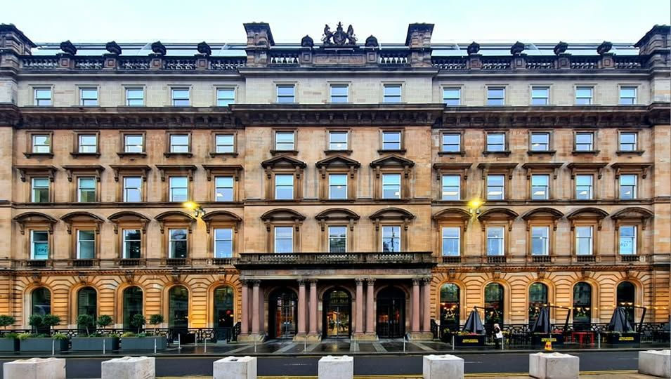 Brown's brasserie & bar on George Square. Ornate multi-story stone building with arches and columns, lit by street lamps. Outdoor seating with umbrellas in front. Overcast sky.