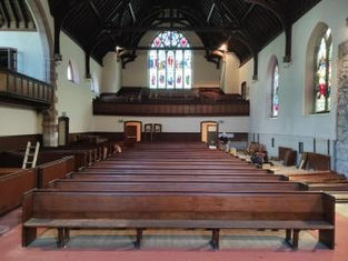 Interior of Kilbarchan church with wooden pews, stained glass windows, and exposed wooden ceiling beams. A ladder leans against the wall.