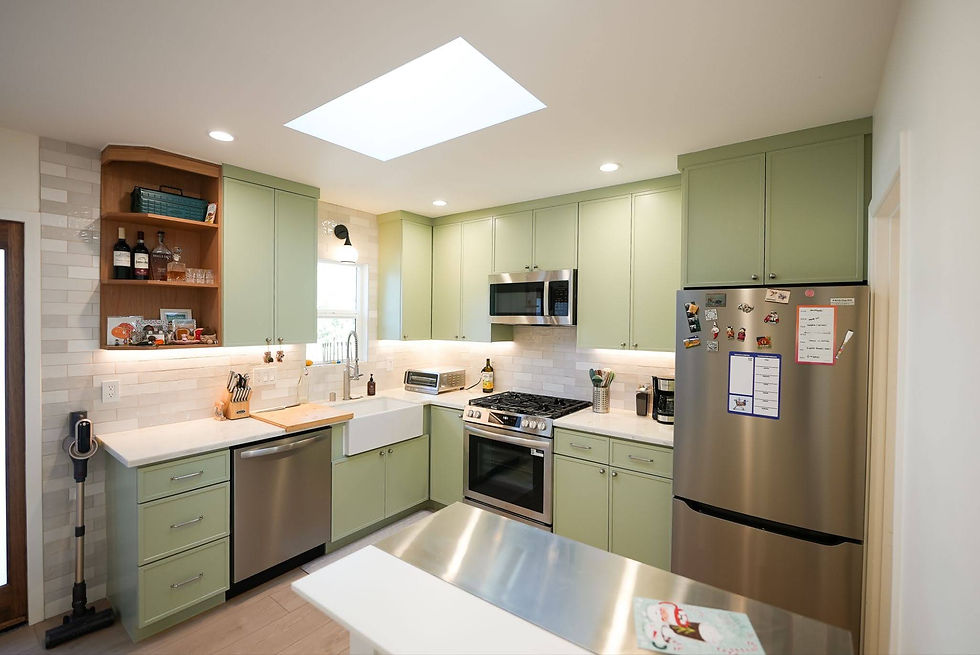 Compact ADU kitchen with sage green cabinets, open shelves, a skylight, and stainless steel appliances.