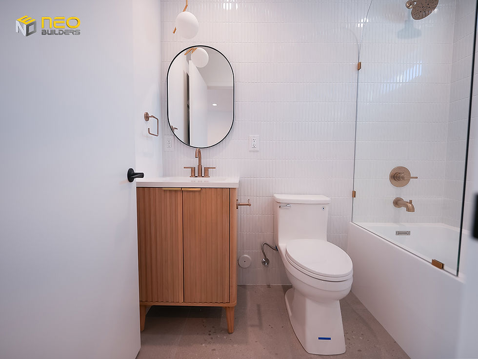 Bathroom in a Crescent Heights garage conversion ADU featuring a custom wood vanity, white vertical tile walls, bathtub with glass shower panel, and brushed brass fixtures.
