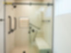Accessible walk-in shower inside a modern Inglewood ADU with grab bars, built-in bench, handheld shower head, and chevron tile extending to the ceiling.