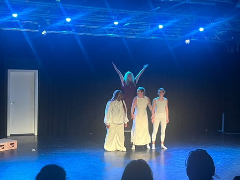 three members of the chorus clothed in white turn to see Medea, clothed in red standing powerfully behind them