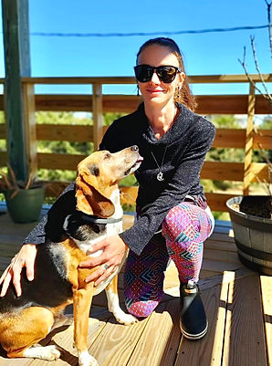 Meg Blue, a slender 30-something with long hair pulled back in a ponytail, dark sunglasses, and a fun pair of leggings, petting a hound dog whose tongue is out