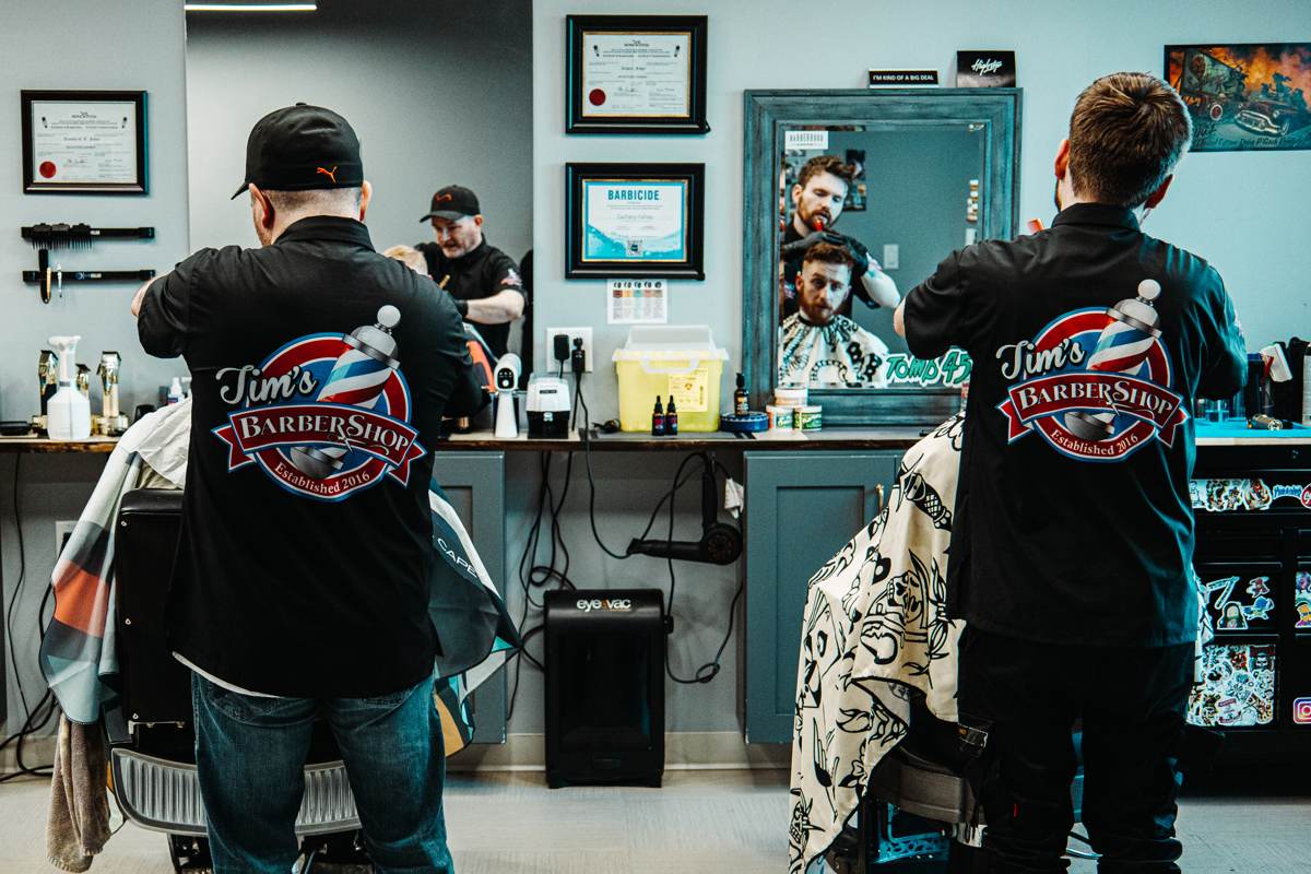 Barbers at Tim’s Barbershop working with customers in front of a wall of mirrors