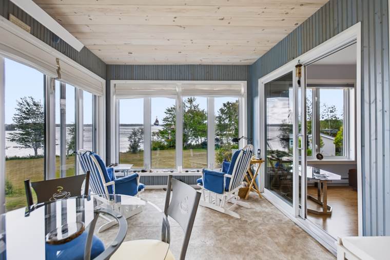 Enclosed sunroom with pale wood ceilings, blue chairs and large windows