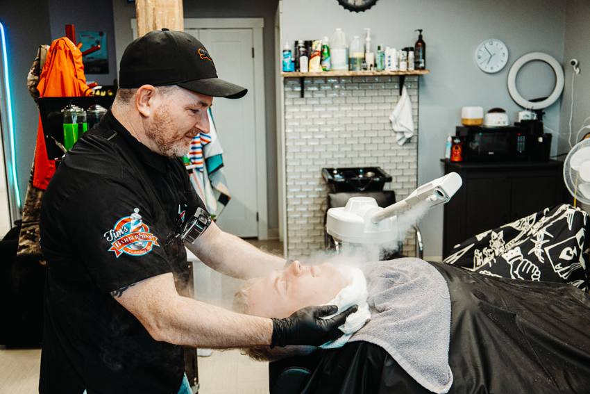 Barber working with shaving foam and a towel beside a chair at Tim’s Barbershop