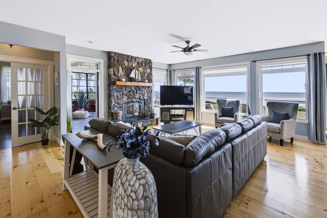 Bright living room with dark sofas, a stone fireplace, wood floors and large windows
