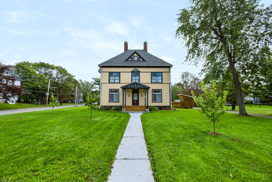 Yellow two-storey home with a front porch, green lawn and mature trees