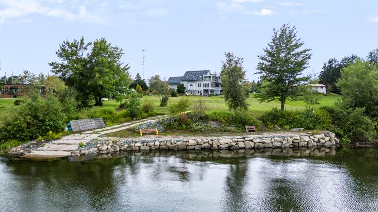 Aerial view of a waterfront home, lawn and stone-edged shoreline